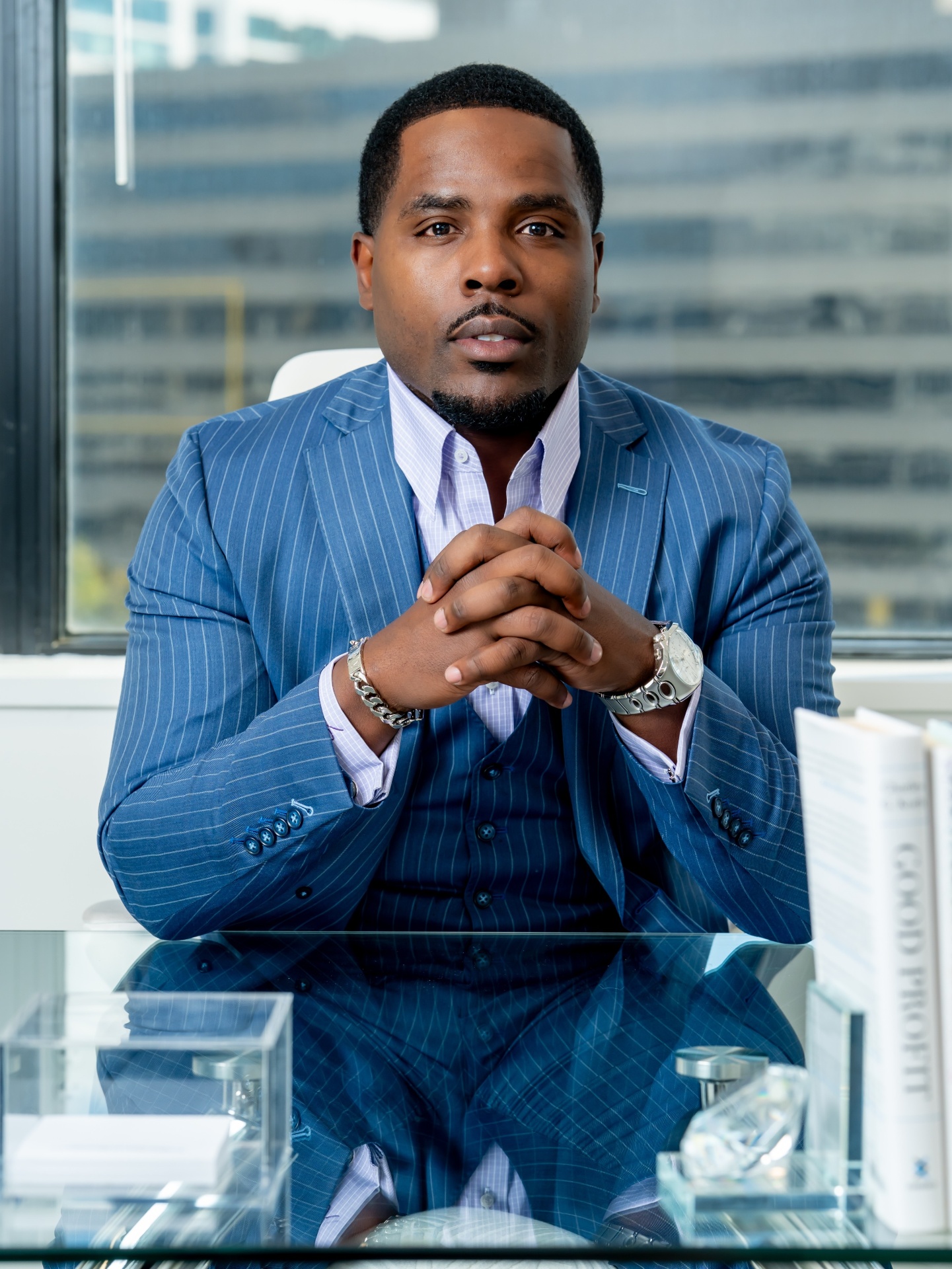 Isiah Williams seated at his desk in a pinstripe suit with the city behind him