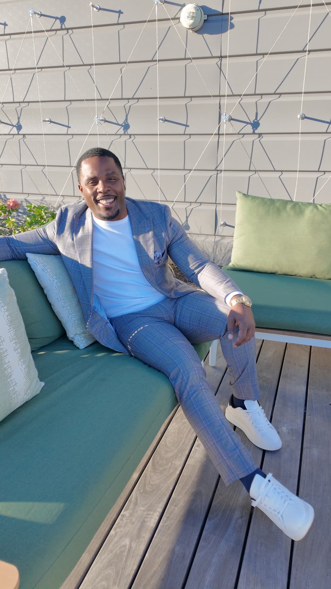 Isiah Williams laughing on a rooftop terrace in a grey plaid suit