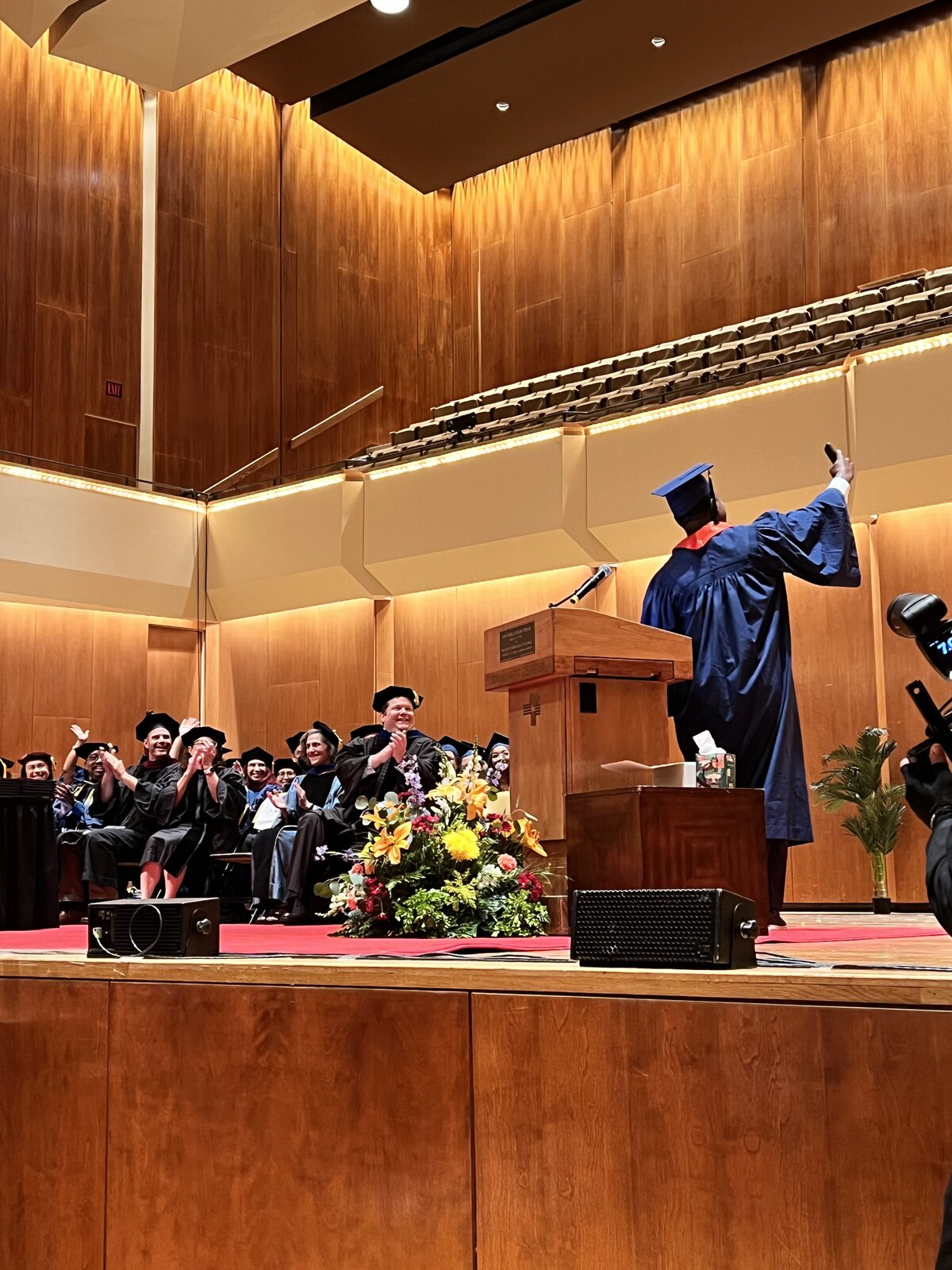 Faculty applauding as Isiah Williams delivers a commencement address in cap and gown