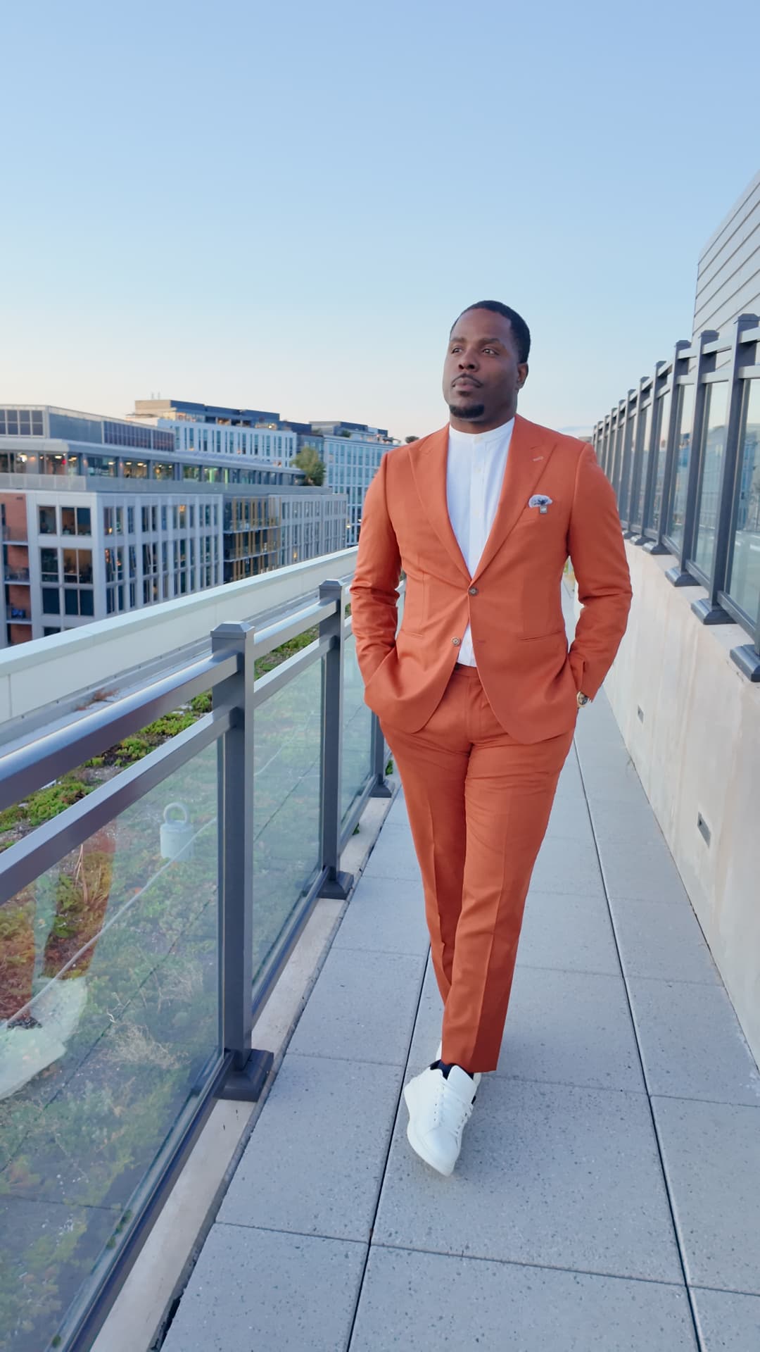 Isiah Williams in a tailored orange suit on a rooftop walkway